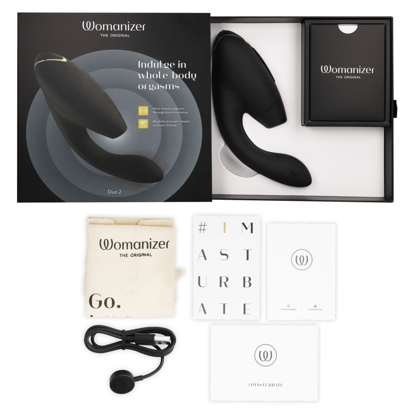Black Womanizer Duo 2 stimulator with ergonomic curves, packaging box, black pouch, charging cable, and manuals laid out.