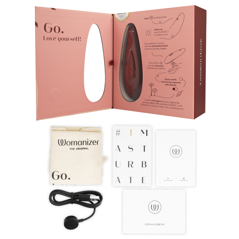 Bordeaux WOMANIZER Classic 2 clitoral stimulator with USB charger, storage pouch, and instructions in open branded packaging.